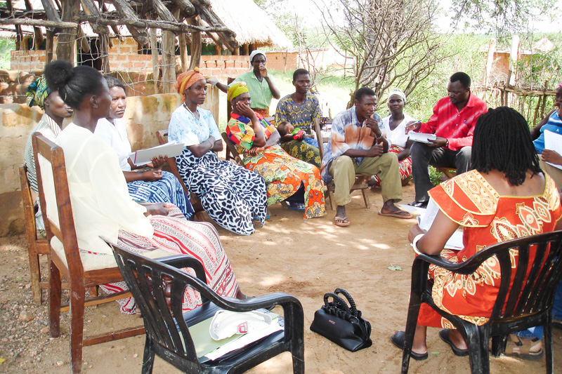 Mutunda (far right) sits with community members in her role as an Akros W.A.S.H. Surveillance officer.