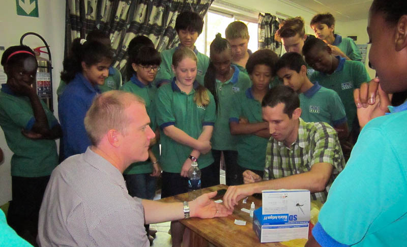 A teacher receives a malaria rapid diagnostic test to demonstrate the process for the students.