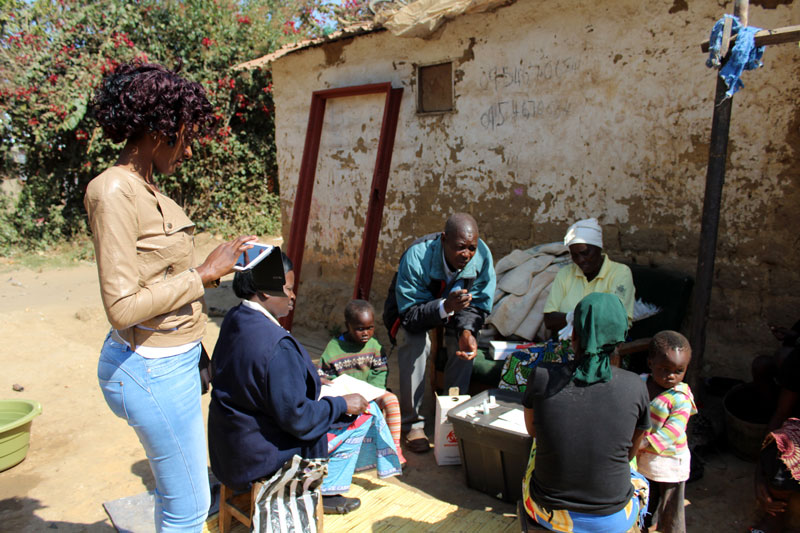 Mwila Sianankange inputs malaria-testing data into DHIS2 software while the reactive team consults with Chainda residents in Lusaka.